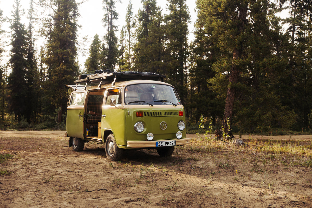 VW-Bus mit beladenem Dachträger beim Camping im Wald