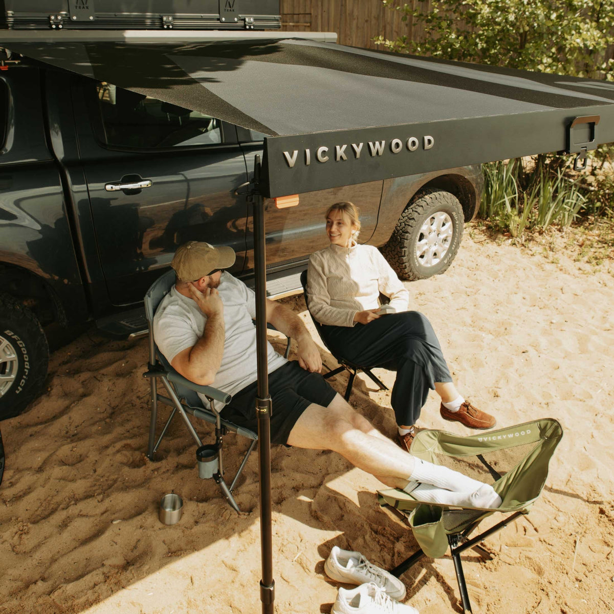 Zwei Personen sitzen im Schatten der ausgezogenen VICKYWOOD Seitenmarkise BRANCH AUTOMATIC 2M neben einem Pick-up