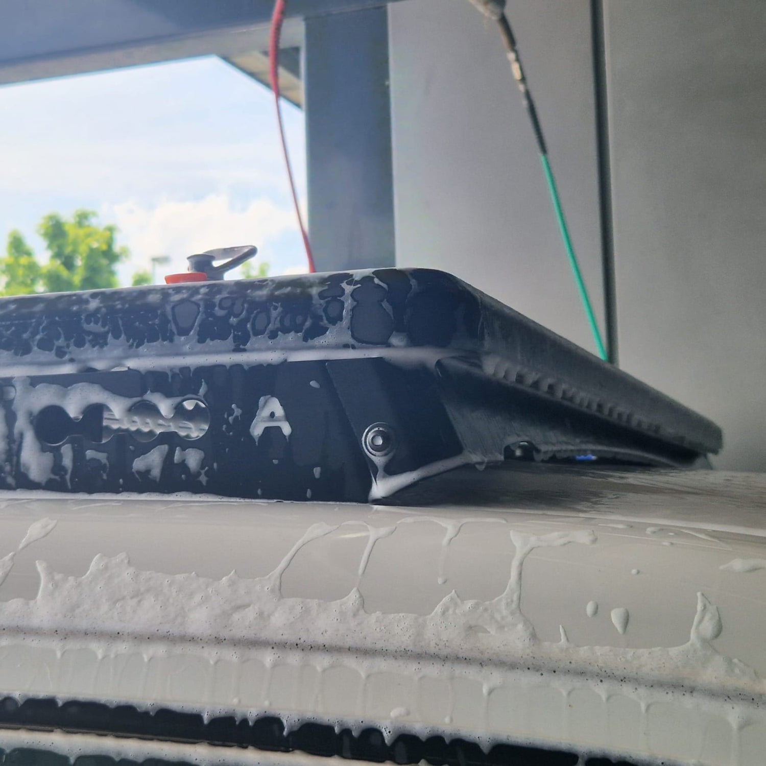 Airholder Dachträger-Windabweiser auf einem weißen Van, mit Aktivschaum bedeckt, während der Reinigung in der Waschanlage.