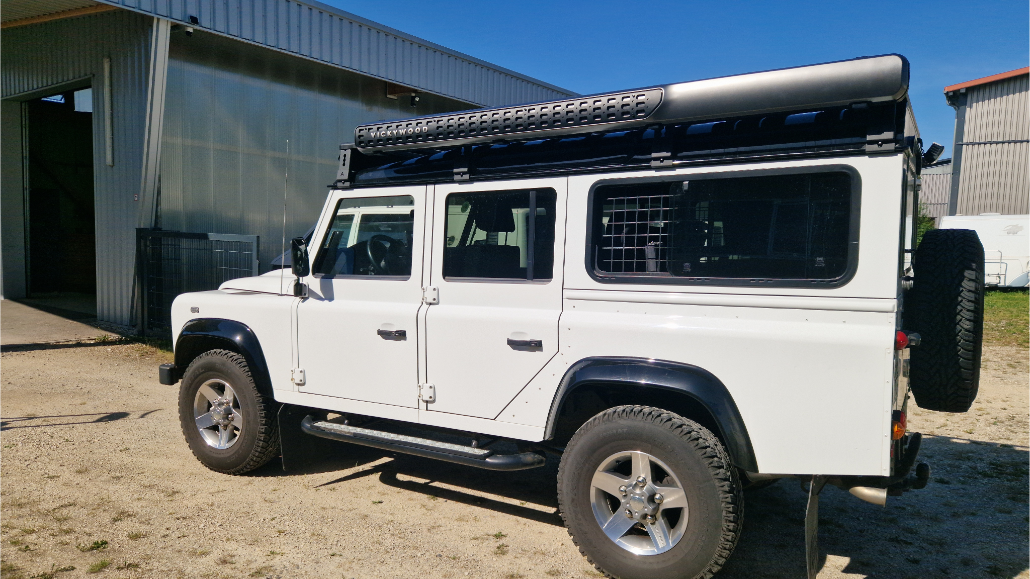 Langer modularer Airholder Aluminium-Dachträger auf einem weißen Land Rover Defender 110 mit einer Vickywood Markise im Hartschalenkoffer