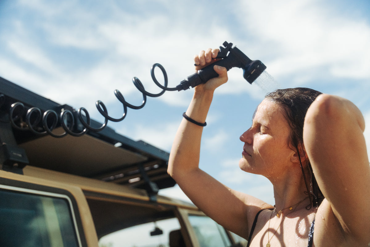 Frau duscht am Camper mit Wasser aus dem VICKYWOOD EVOTANK auf dem Dach
