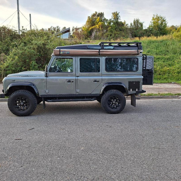 Grauer Land Rover Defender 110 mit offener Hecktür, Leiter und kurzem Airholder Aluminium-Dachträger inklusive Markise