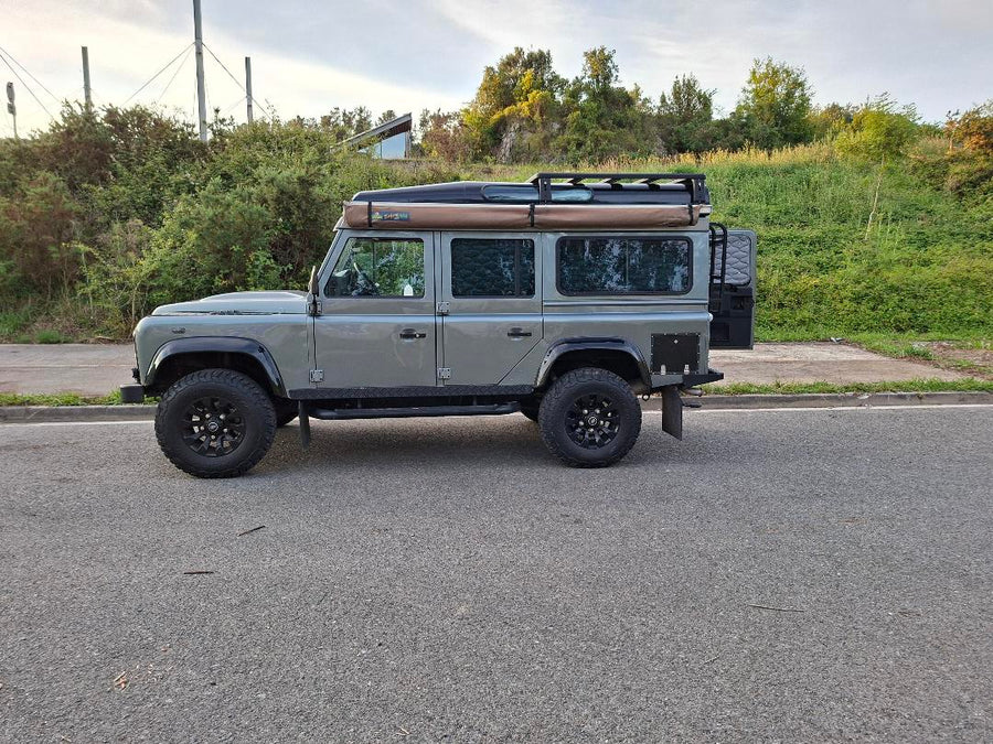 Grauer Land Rover Defender 110 mit offener Hecktür, Leiter und kurzem Airholder Aluminium-Dachträger inklusive Markise