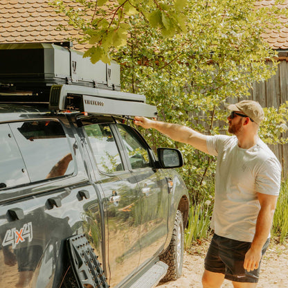 Mann zieht die VICKYWOOD Seitenmarkise BRANCH AUTOMATIC 2M an einem Pick-up mit Dachträger von Hand aus